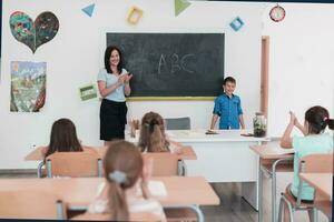 elementair school. de vrouw leraar helpen de kind leerling terwijl schrijven de antwoord Aan de schoolbord. foto