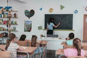 elementair school. de vrouw leraar helpen de kind leerling terwijl schrijven de antwoord Aan de schoolbord. foto