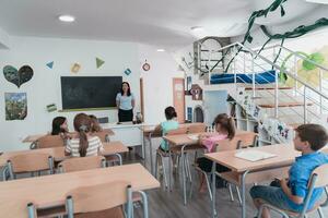 elementair school. de vrouw leraar helpen de kind leerling terwijl schrijven de antwoord Aan de schoolbord. foto