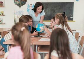 vrouw leraar met kinderen in aardrijkskunde klasse op zoek Bij wereldbol. kant visie van groep van verschillend gelukkig school- kinderen met wereldbol in klas Bij school. foto