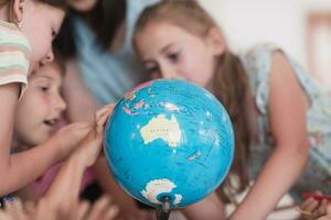 vrouw leraar met kinderen in aardrijkskunde klasse op zoek Bij wereldbol. kant visie van groep van verschillend gelukkig school- kinderen met wereldbol in klas Bij school. foto