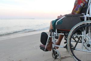 oude man in een rolstoel kijkt vanaf het strand naar de zee foto