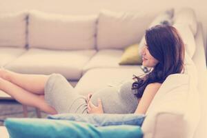 zwanger vrouw zittend Aan sofa Bij huis foto