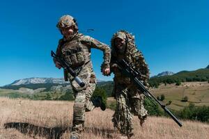 een scherpschutter team ploeg van soldaten is gaan undercover. scherpschutter assistent en team leider wandelen en het richten in natuur met geel gras en blauw lucht. tactisch camouflage uniform. foto