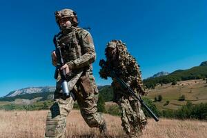 een scherpschutter team ploeg van soldaten is gaan undercover. scherpschutter assistent en team leider wandelen en het richten in natuur met geel gras en blauw lucht. tactisch camouflage uniform. foto