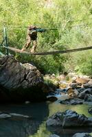 een leger Mens of airsoft speler in een camouflage pak sluipen de touw brug en doelen van een scherpschutter geweer- naar de kant of naar doelwit. foto