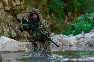 een leger Mens of airsoft speler in een camouflage pak sluipen de rivier- en doelen van een scherpschutter geweer- naar de kant of naar doelwit. foto