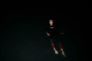 triatlonatleet die in donkere nacht zwemt die wetsuit draagt foto