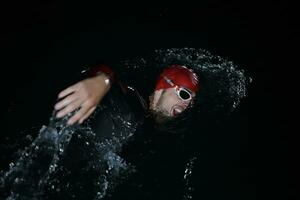 triatlonatleet die in donkere nacht zwemt die wetsuit draagt foto