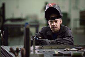 portret van jong professioneel zwaar industrie ingenieur. arbeider vervelend veiligheid hesje en harde hoed glimlachen Aan camera. in de achtergrond ongericht groot industrieel fabriek foto