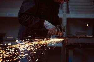 zware industrie engineering fabrieksinterieur met industriële werknemer die haakse slijper gebruikt en een metalen buis snijdt. aannemer in veiligheidsuniform en bouwhelm voor het vervaardigen van metalen constructies. foto