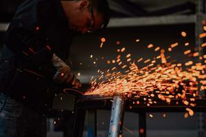 zware industrie engineering fabrieksinterieur met industriële werknemer die haakse slijper gebruikt en een metalen buis snijdt. aannemer in veiligheidsuniform en bouwhelm voor het vervaardigen van metalen constructies. foto