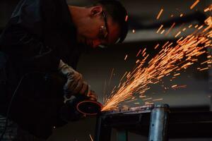 zware industrie engineering fabrieksinterieur met industriële werknemer die haakse slijper gebruikt en een metalen buis snijdt. aannemer in veiligheidsuniform en bouwhelm voor het vervaardigen van metalen constructies. foto