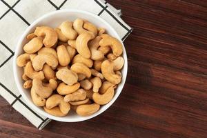 bovenaanzicht van cashewnoten in witte kom op tafel, plat gelegd foto