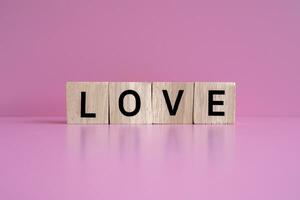 houten blokken het formulier de tekst liefde tegen een roze achtergrond. foto