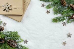 Kerstmis Spar boom takken vlak leggen met pijnboom kegels, omhulsel geschenk dozen en decoratie Aan sneeuw achtergrond. creatief samenstelling met grens. top visie. kopiëren ruimte. foto