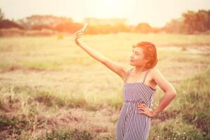 jonge vrouw staande met behulp van haar smartphone selfie in het grasveld. foto