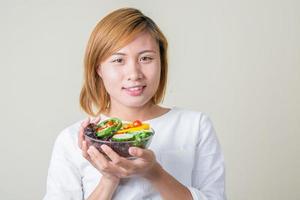 mooie vrouw met een kom verse groentesalade glimlacht naar de camera foto