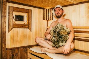 een Mens met een bezem in zijn hand- is ontspannende in de sauna foto