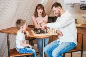 gelukkig familie moeder, vader en hun zoon spelen schaak in de kamer foto
