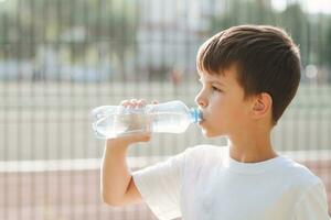 schattig kind drankjes water van een fles Aan de straat in zomer foto