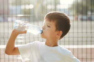 schattig kind drankjes water van een fles Aan de straat in zomer foto