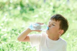 schattig kind drankjes water van een fles Aan de straat in zomer foto