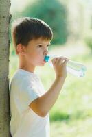 schattig kind drankjes water van een fles Aan de straat in zomer foto