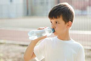 schattig kind drankjes water van een fles Aan de straat in zomer foto