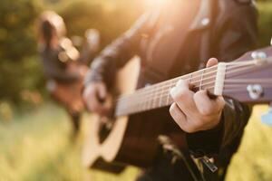 vrouw en Mens spelen akoestisch gitaar in natuur Bij zonsondergang foto
