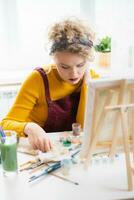 vrouw zittend in voorkant van een schilderij en schilderij met borstels Aan canvas Bij huis foto