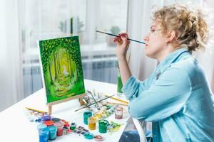 vrouw zittend in voorkant van een schilderij en schilderij met borstels Aan canvas Bij huis foto