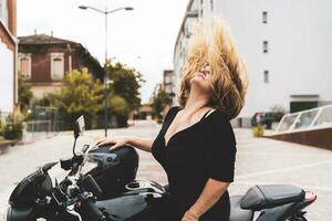 midden- oud fietser vrouw gooien haar blond haar- terug rijden modern zwart motorfiets foto