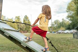 weinig schattig meisje is beklimming Aan een houten plank in een buitenshuis park foto