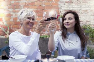 moeder en volwassen dochter proeverij wijn zittend buitenshuis foto