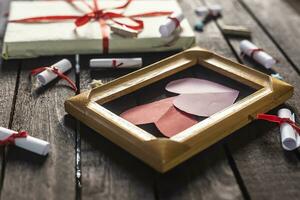 vlak leggen romantisch achtergrond. geschenkdoos, gerold wens papieren, en houten kader met papier harten Aan donker hout bord. foto