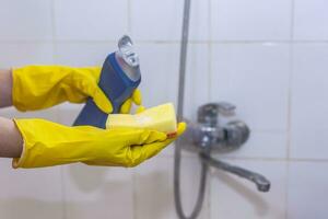 vrouw in handschoenen zetten schoonmaak chemie naar de spons en willen naar schoon omhoog de badkamer foto