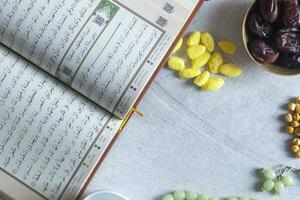 heilig koran, rozenkrans, iftar snoepgoed en droog fruit met een kop van water. visie van bovenstaande. vlak leggen foto