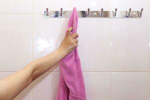 jong vrouw na douche. vrouw nat hand- nemen haar roze badjas hangende Aan een haak. nemen badjas na douche foto