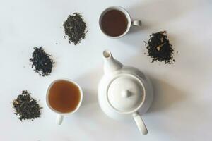 thee reeks met wit keramisch thee pot en andere thee ingrediënten Aan de wit. vlak leggen visie van divers droog thee en theepot. visie van bovenstaande. ruimte voor uw tekst foto