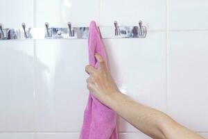 jong vrouw na douche. vrouw nat hand- nemen haar roze badjas hangende Aan een haak. nemen badjas na douche foto