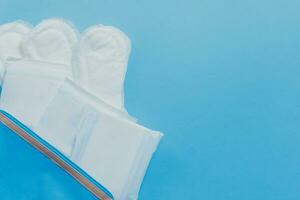 vrouwelijk hygiëne producten. vrouwen zak en sanitair stootkussens Aan blauw achtergrond foto