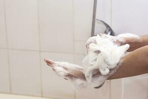 vrouw het wassen handen met een spons in de badkamer. vrouw het wassen armen met een schuimend spons in de bad. lichaam zorg en schoon concept foto