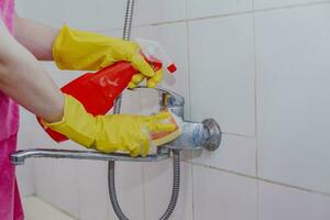 huisvrouw schoonmaak badkamer kraan en douche tik. hulp in de huishouding in geel beschermend handschoenen het wassen vuil bad tik. handen van vrouw het wassen bad foto