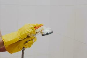 vrouw in rubber handschoenen schoonmaak de douche hoofd. dienstmeisje het wassen metalen hoofd van de douche. huisvrouw schoonmaak omhoog in de badkamer foto