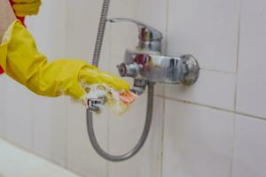 huisvrouw schoonmaak badkamer kraan en douche tik. hulp in de huishouding in geel beschermend handschoenen het wassen vuil bad tik. handen van vrouw het wassen bad foto