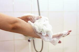 vrouw het wassen handen met een spons in de badkamer. vrouw het wassen armen met een schuimend spons in de bad. lichaam zorg en schoon concept foto