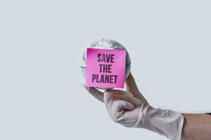 hand- in medisch handschoenen houdt een wereldbol met Notitie - opslaan de planeet foto