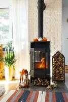 helder zonnig interieur van de huis met zwart metaal staal haard fornuis met brand en brandhout met halloween decor en herfst humeur. knus huis haard in interieur met binnen- ingemaakt fabriek foto