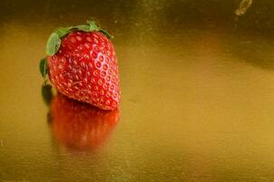 een aardbei is zittend Aan een gouden oppervlakte foto